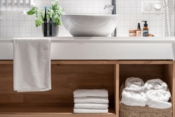 Wooden countertop with shelf for storage fresh and white terry towels. Wicker laundry basket under washbasin in modern hotel bathroom. Clean textile for body hygiene in comfort apartment