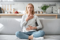 Concept of mental health. Woman sitting on couch and doing calming breathing exercises after panic attack. Female inhaling and exhaling to deep breath. Self-control, anxiety relief concept