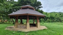 A brown octagonal pavilion built on a public green lawn for people to rest.