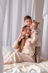 Two happy sibling hugs their young mother, happy family laughing and smiling on the bed.