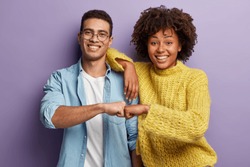 Young diverse couple give fist bump, agree to bring plan to life, smile broadly, have mixed race relationships, have good friendly partners, isolated over purple wall. I agree with you concept