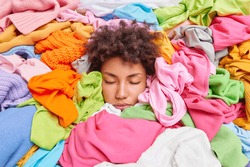 Clothing dilemma. Curly haired woman buried in stack of multicolored clothes throws clothing above head keeps eyes closed feels tired of doing housework. Daily domestic routines. Delcuttering