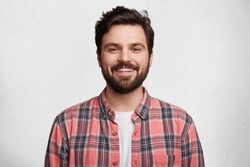 Smiling bearded young male model rejoices coming weekends, dressed casually, isolated over white background. Positive pleased student being in good mood after successfully passed exams at college