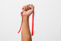 The hands of a man holding a red and white ribbon as a symbol of the Indonesian flag. Isolated on gray background