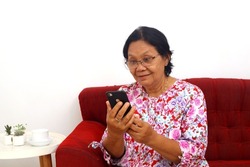Surprised elderly asian woman sitting while reading a news from her cellular phone. Isolated