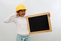 Happy Asian little girl in the construction helmet as an engineer standing while holding blackboard and successful gesture. Isolated on white
