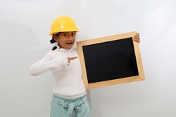 Happy Asian little girl in the construction helmet as an engineer standing while pointing a blackboard. Isolated on white