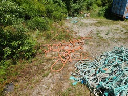 A wooden pallet that is full of thick, colorful ropes that are all tangled, disheveled, and knotted together. The ropes are strong fisherman's rope that are blue, gray, orange, and white.