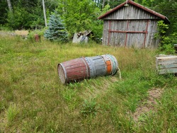 Old barrels stacked together and turned over in grass. They're made of wood and are different colors. The wooden containers are weathered and their paint is starting to chip.
