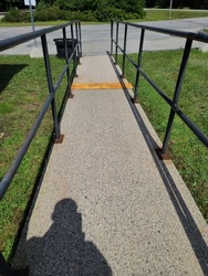 The shadow of a man walking his dog down the cement walkway with black railings on both side. The sidewalk is in a suburban community.