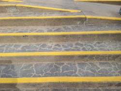 A shot of stairs with cracked cement and yellow paint on edges.