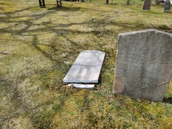 The back of a broken headstone that is cracked through lying on the grass.