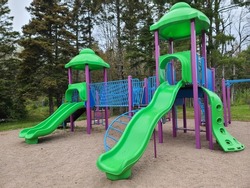 A bunch of playground equipment at a park. The metal and plastic jungle gym are bright shades of green, blue, and purple.