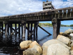 A closeup of an old wooden bridge extending from a rocky area along a beach.