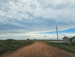 A red dirt road under a cloudy afternoon sky with a lighthouse in the far distance.