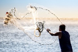 A fisherman casting a net into the water during on a golden horizon