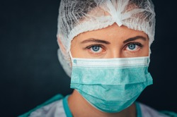 Protection against contagious disease, coronavirus. Portrait Photo. Female medical worker wearing protective face mask, head cover and suit inside hospital ward
