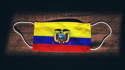 Ecuador National Flag at medical, surgical, protection mask on black wooden background. Coronavirus Covid–19, Prevent infection, illness or flu. State of Emergency, Lockdown