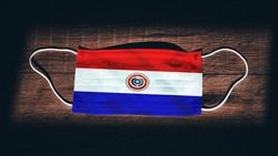 Paraguay National Flag at medical, surgical, protection mask on black wooden background. Coronavirus Covid–19, Prevent infection, illness or flu. State of Emergency, Lockdown