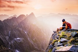 Young male hiker with backpack relaxing on top of a mountain during calm summer sunset - scenery from vacation - photo with space for your montage.