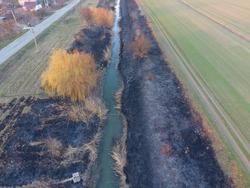 Irrigation canal with burned reeds along the shore. Ashes from the grass