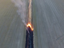 Burning dry grass along the irrigation canal. Smoke and the flame of dry grass. Burnt dry grass