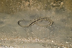 The sign of infinity on the sea. Coastal sand on the beach. The symbol of infinity.