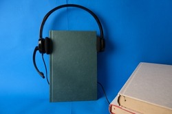 Concept of Audiobook on white background. Headphones put over green hardback book, with blue background