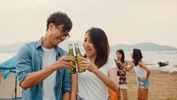 Group of Asia best friends teenagers focus on couple toast beer enjoy camping party with happy moments together beside tents in national park. On the background beautiful nature, mountains and lake.