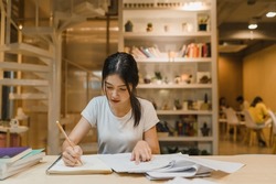 Asian student women reading books in library at university. Young undergraduate girl do homework, read textbook, study hard for knowledge on lecture desk at college campus overtime night.