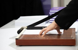 A young man using a Paper cutter to make a book in the office. cutting paper on desk. 
office equipment