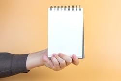 hand holding blank page notebook on yellow background. with copy space