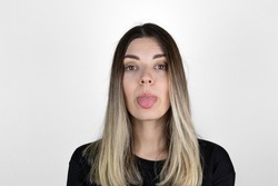 Young woman sticking out tounge, close up portrait. Teasing you through camera while isolated with white background. 