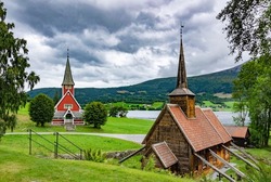 Rodven  old and new churches. Medieval wooden viking era church in Norway. Dramatic cloudy sky, green grass and trees, ancient wooden walls, green mountain slopes and grey fjord water on th background