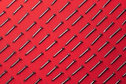 lot of black steel nails, on red background, arranged diagonally perfectly, concept of perfectionism and equality
