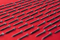 lot of black steel nails, on red background, arranged diagonally perfectly, concept of perfectionism and equality

