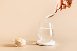 Woman adds psyllium fiber to glass of water on beige background. Superfood for healthy intestines and gluten free diet.