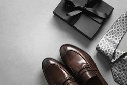 Father's Day greeting card with gift box. Set of classic mens clothes - brown loafers shoes, tie and gift on gray background. Men's accessories set. Top view. Copy space.