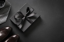 Greeting card with gift for father on black background. Set of classic mens clothes - brown shoes, tie and gift. Happy Fathers Day. Men's accessories set. Top view. Copy space.