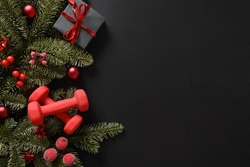 Christmas sport composition with gift and two red sports dumbbells on black background. Top view with copy space. Fitness, sport and healthy concept. Christmas greeting card. Winter sale.
