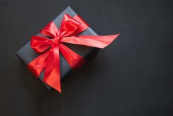 Gift box wrapped in black paper with red ribbon on black surface. Top view with copy space.