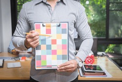 Young man holding and point to a color chart for home design. Graphic designers working on color chart at modern office.