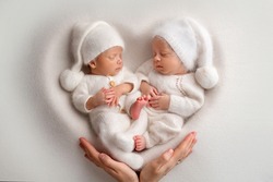 Tiny newborn twin boys in white bodysuits on a white background. Newborn twins sleep next to their brother on the background of the heart. Parents mother holds children with their hands with palms.