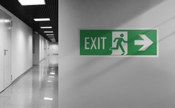 Emergency exit sign. Interior internal corridor of modern office. Corridor with light walls, black ceiling and shiny floor. Soft focus.