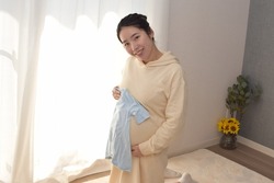 A pregnant young woman is looking forward to the birth of her baby with her blue baby clothes.