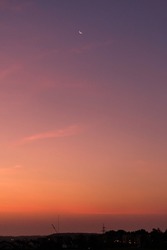 Waning crescent moon on beautiful purple, pink, orange skies over waking city at sunrise