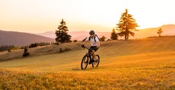 Professional mountain bike cyclist riding a forest trail at sunset. 