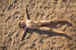 the boy lies on the sand in the pose of a star and smiles, top view