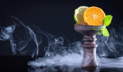 fruit hookah bowl with tobacco, tangerine, lime, mint and smoke on black background