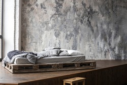 Unfilled bed made of wooden blocks with beige bedding in the bedroom against a wall with Venetian stucco. Scandinavian style
